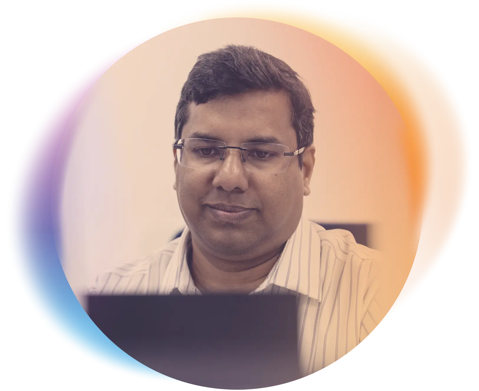 A man wearing glasses and a striped shirt is focused on his laptop, seated indoors with a soft gradient circular overlay in warm orange and cool blue tones.